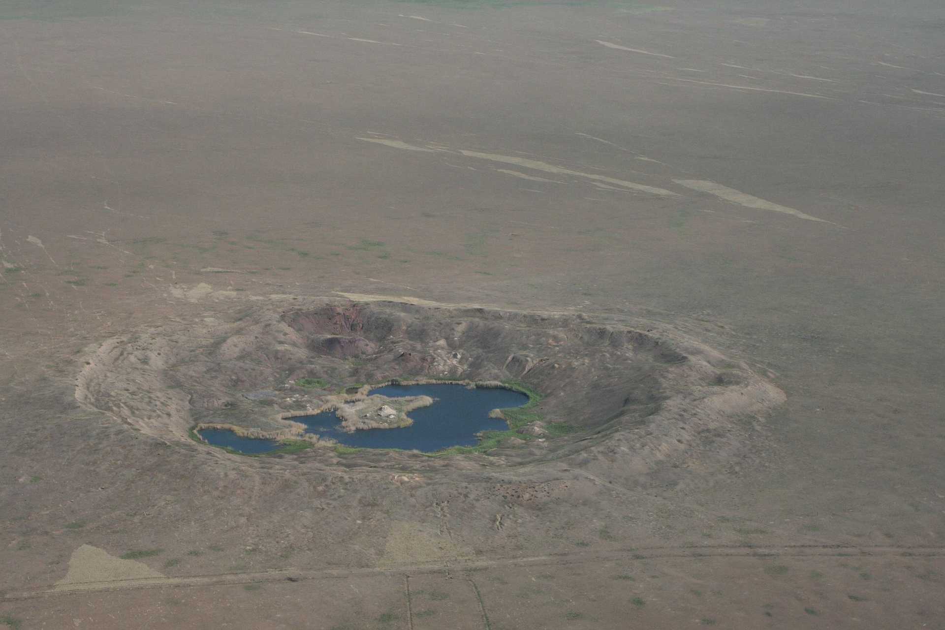 Photograph of a large, circular crater. The image shows the crater’s steep, rugged edges and the surrounding terrain. The crater is a former USSR nuclear test site Semipalatinsk (today's Kazakhstan).