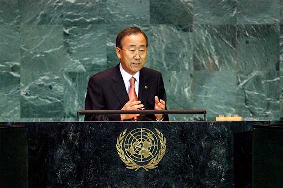 Ban-Ki Moon speaks at a desk with UN logo in front of a green wall.