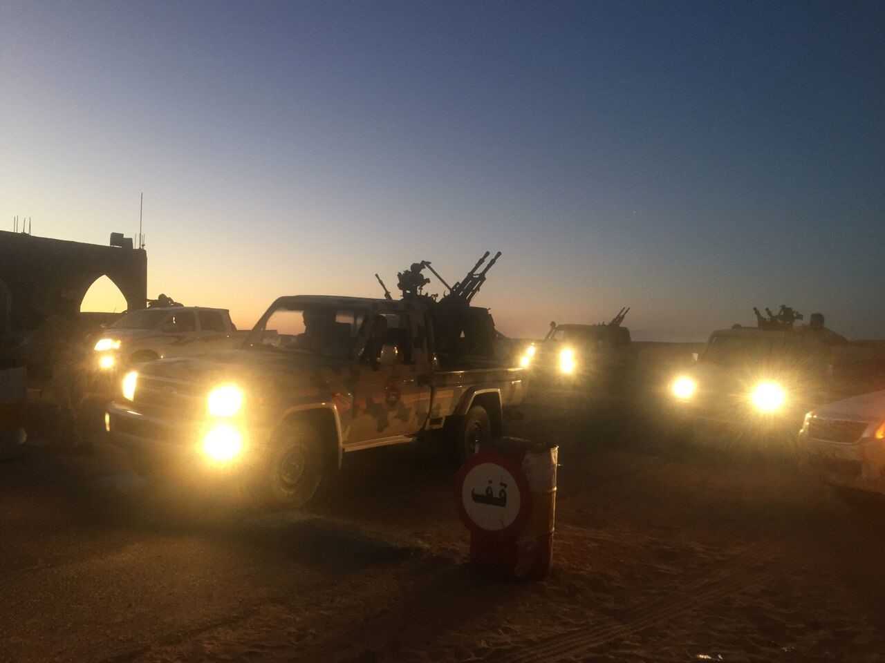 Photo of trucks in a desert landscape. There are weapons on the beds of the trucks.