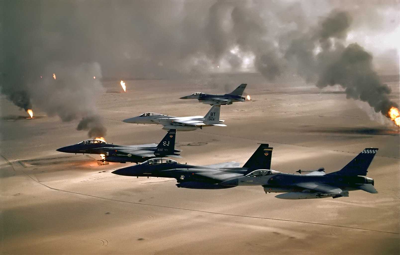 Military jets flying over a desert landscape with smoke rising from oil well fires in the background.