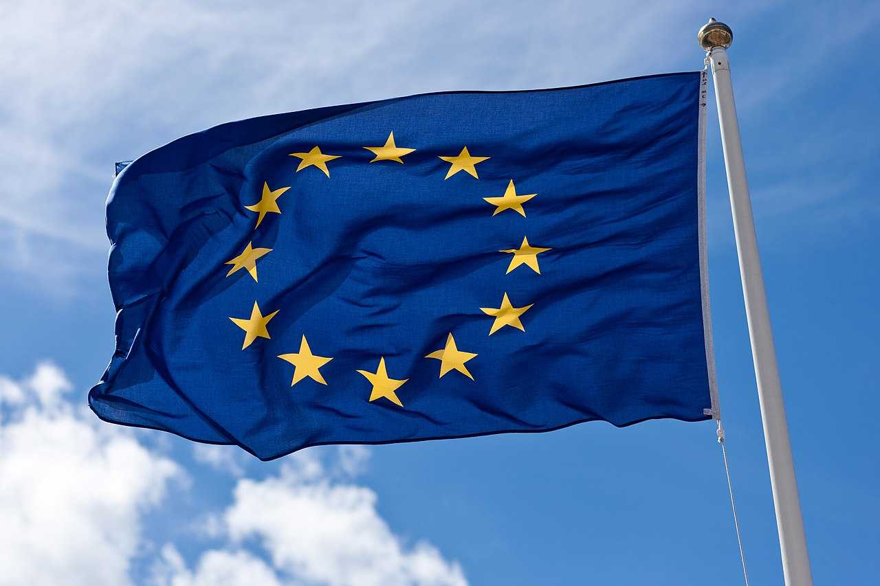 The EU flag with its 12 golden stars on a blue background flying in the wind.