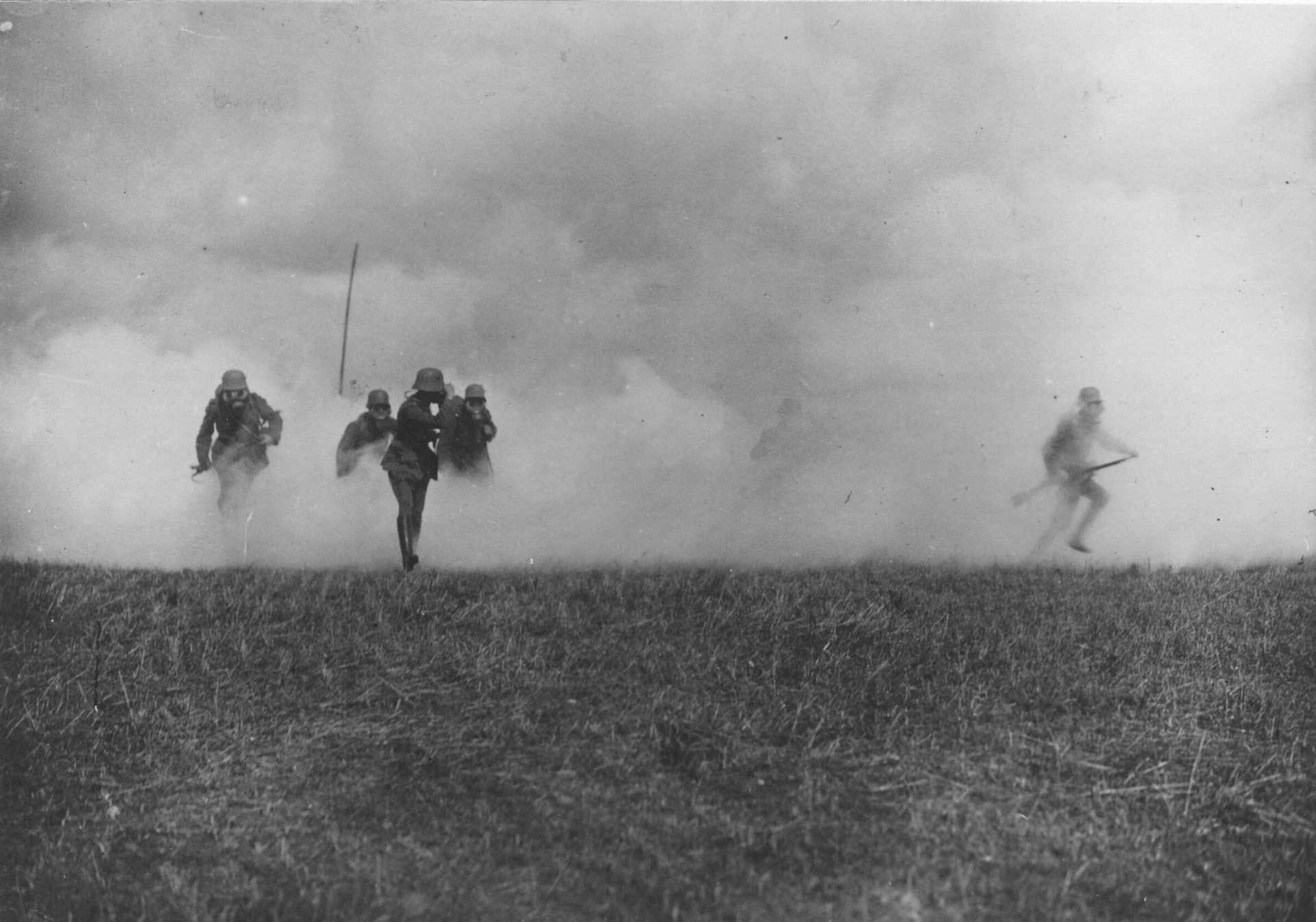 Historic photograph showing soldiers with gas masks running from dark clouds on a field towards the camera.