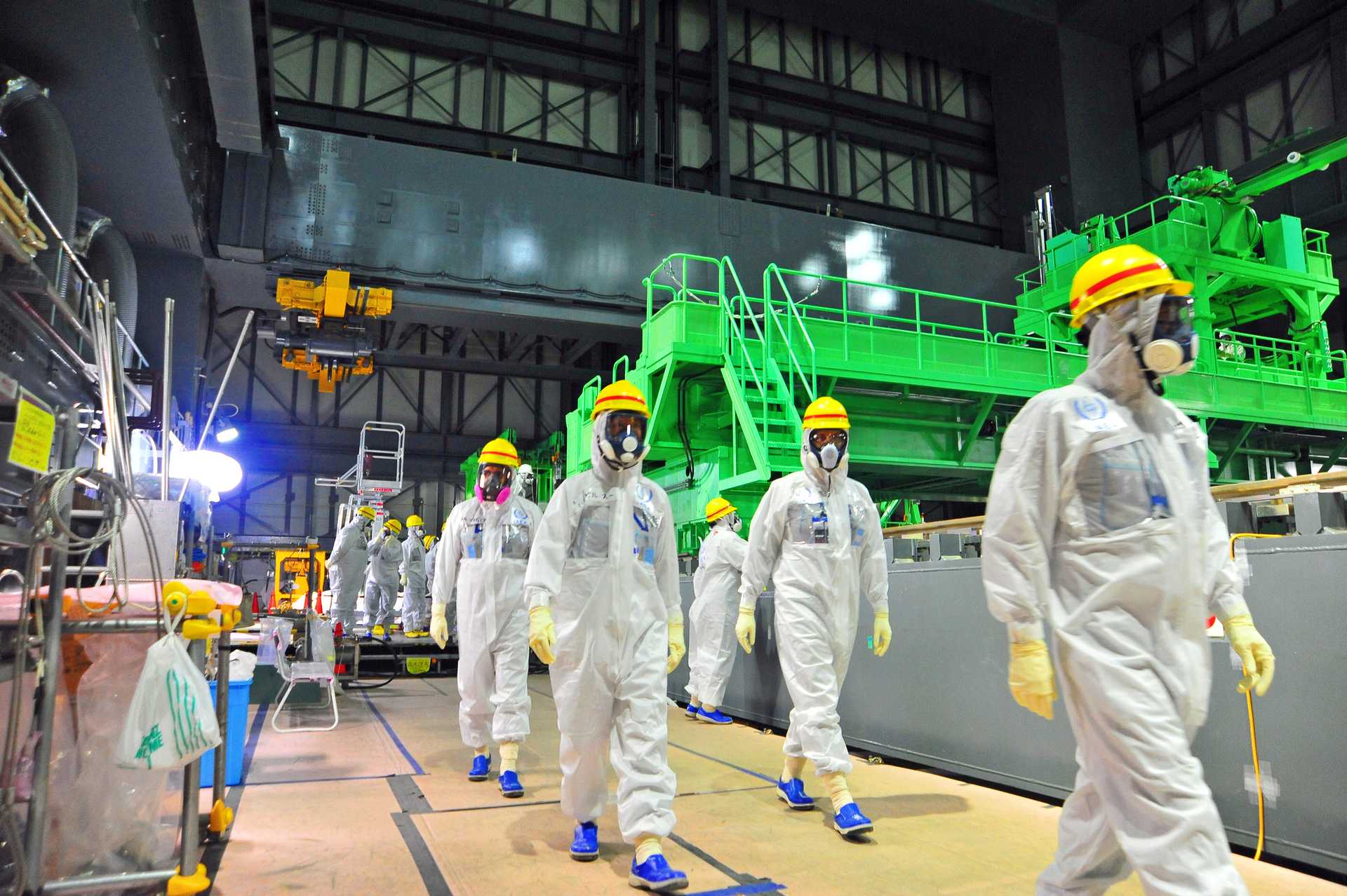 Photography of people in hazmat suits, helmets and masks walking through a factory building.
