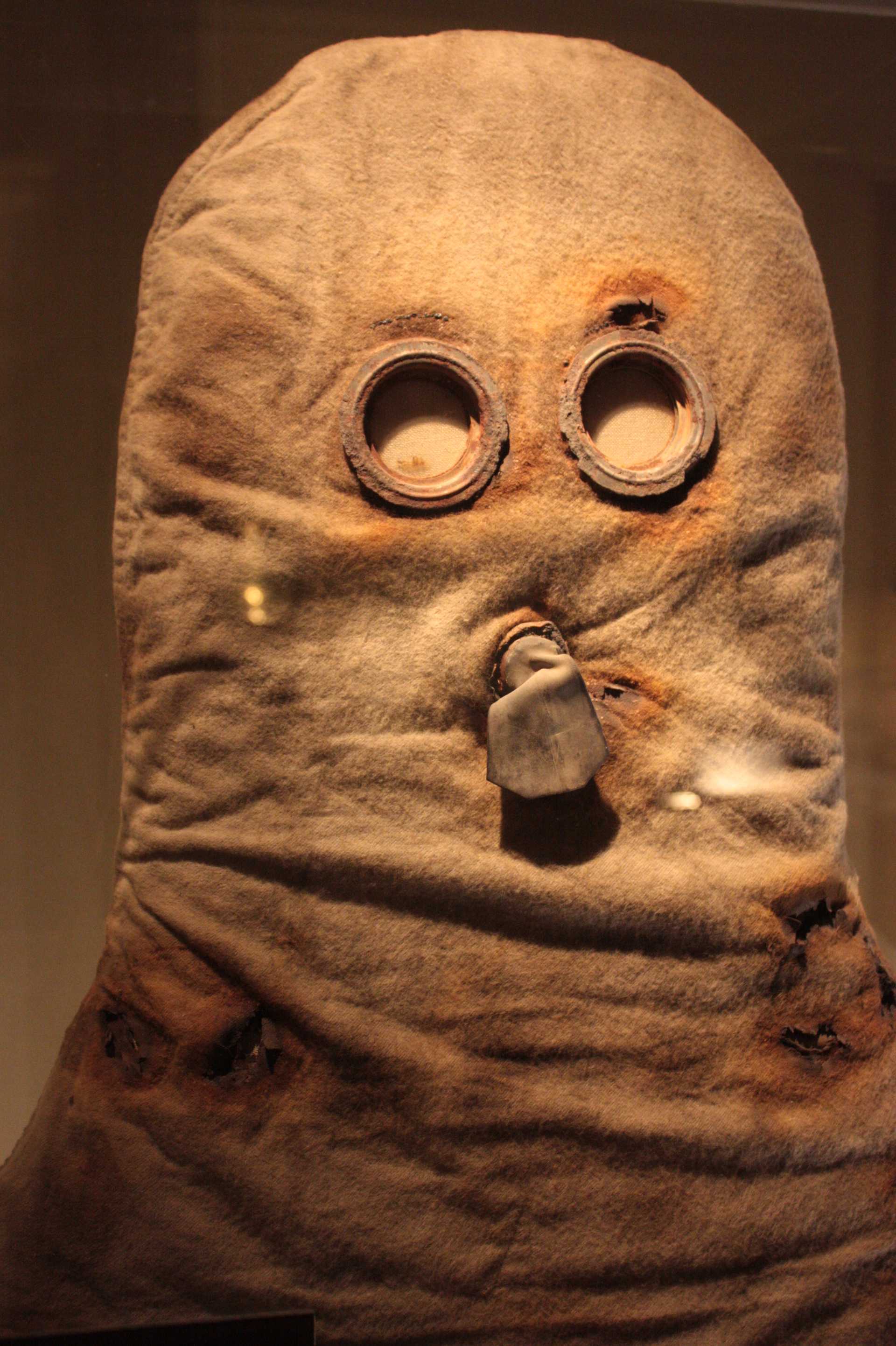 A photograph of a World War I-era gas mask on display, showcasing its historical design in a museum setting.