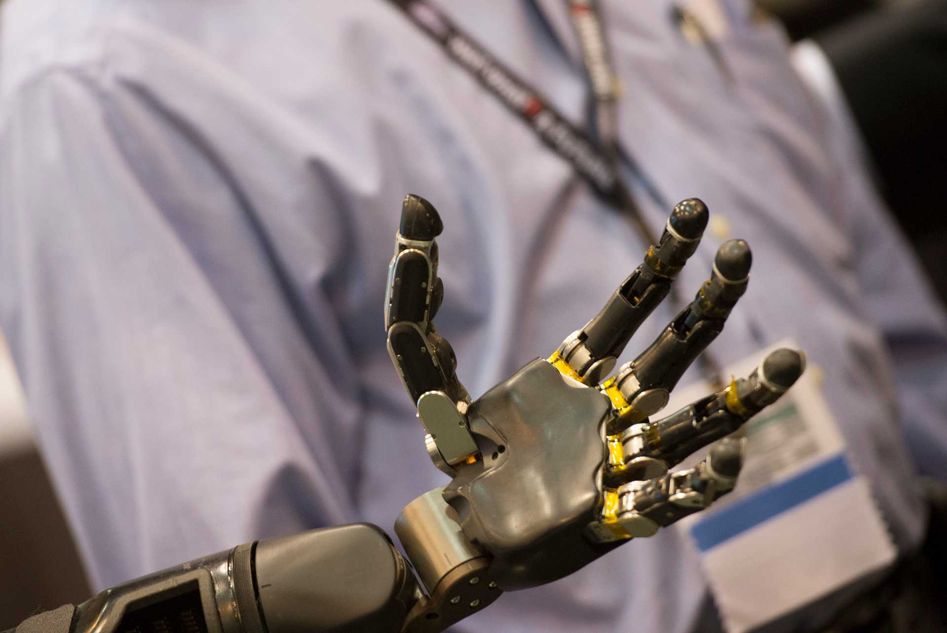 An open robotic hand with the torso of a person blurry in the back
