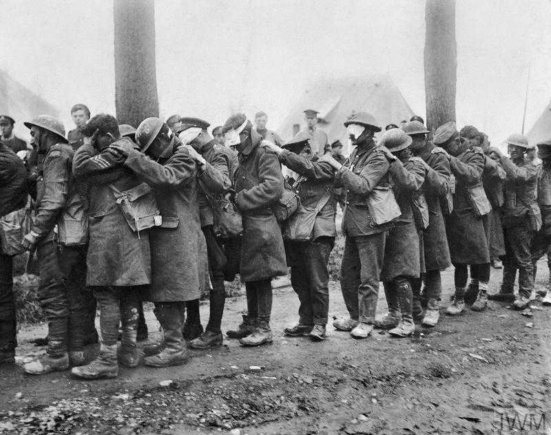 A historic photograph of a line of British troops during the First World War. Most of the men are blindfolded for medical reasons and have their hands on the shoulders of the man in front of them.